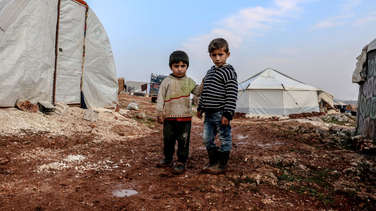 gallery-1 Two children standing in a muddy Syrian refugee camp in Idlib.