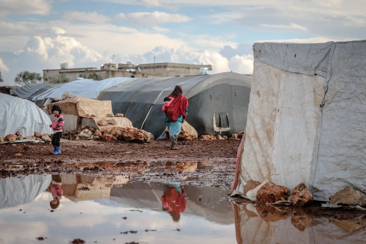 A refugee camp in Idlib, Syria, showing tents and muddy conditions with people nearby.